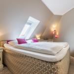 Schlafzimmer mit Dachschrägen, Dachfenster und Bett mit rosa Kissen.