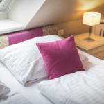 Schlafzimmer mit Bett, Kissen und Nachttisch unter Dachschrägen.