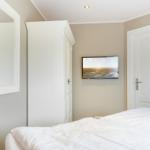 Schlafzimmer mit Bett, Spiegel, Kleiderschrank und Wandfernseher.