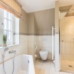 Badezimmer mit Badewanne, Dusche und Toilette. Fenster mit Pflanze.