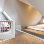 Schlafzimmer mit Dachschräge, Bett, Fenster und Sitzgelegenheit.