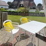 White table and two chairs with yellow cushions on terrace. Background: lawn and thatched house.