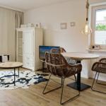 Dining room with round table, chairs, and TV. Windows, curtains, and wooden floor.