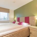 Schlafzimmer mit Doppelbett, Fenster mit Blick und Stehlampe.