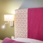 Bettkopfteil mit rosa Decke und Wandlampe.