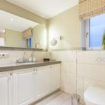 Badezimmer mit Waschbecken, Spiegel und Toilette. Fenster mit Pflanze.