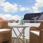 Terrasse mit zwei Stühlen und Tisch. Im Hintergrund sind Gebäude und Himmel zu sehen.