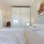 Schlafzimmer mit weißem Bett, Kleiderschrank und Wandbild.