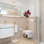 Badezimmer mit Dusche, Waschbecken und Toilette. Mit Spiegel und Orchidee.