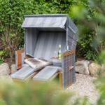 Garden lounger with canopy, drink, and fur blanket between shrubs and stones