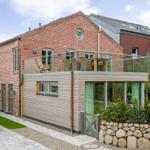 Red brick house with balcony and wooden cladding. Garden with stone wall and plants.