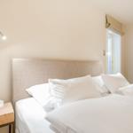 Bedroom with bed, nightstand, and wall lamp. Window and wooden panels visible.