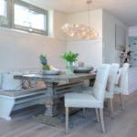 Dining room with wooden table, bench, and chairs. Wall with fish motif. Ceiling light and windows.