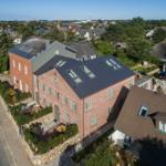 Red brick house with dark roof and multiple skylights. Surrounded by greenery and a paved path.