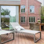Deck with loungers, table and chairs in front of brick house