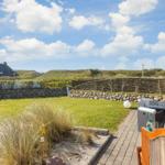 Terrasse mit Sitzgelegenheiten und Blick auf grünen Garten und Strandhaus im Hintergrund.