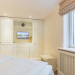 Schlafzimmer mit weißem Schrank, Fernseher und Fenster mit Blick auf Gras.