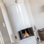 Weiße Kachelöfen mit brennendem Feuer, Kaminutensilien und Korb neben einer Tür.