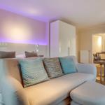 Bedroom with sofa and modern kitchen area in the background.