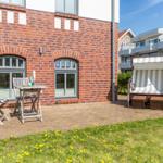Terrace with table, chairs, and beach chair in front of red brick house.
