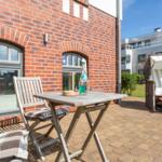 Terrace with table, chairs, and lounge chair in front of red brick house.