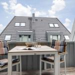 Terrasse mit Tisch und zwei Stühlen. Blick auf ein Haus mit Schiebedachfenstern.