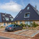 Moderne Ferienhaus mit dunklem Dach und gepflastertem Hof. Ein Auto parkt auf dem Hof.