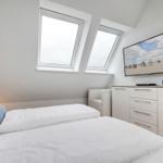 Schlafzimmer mit Dachfenstern, Bett, TV und Schrank.