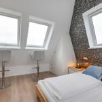 Schlafzimmer mit Dachschrägen, drei Fenstern und einem Bett mit Kissen.