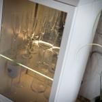 Wein- und Champagnergläser im beleuchteten Schrank neben einer Pflanze.