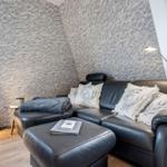 Schwarzes Ledersofa mit Kissen und Beistelltisch vor texturiertem Wandpaneel.