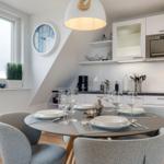 Küche mit Esstisch, weißen Schränken und Fenster. Tisch mit Geschirr und Gläsern gedeckt.