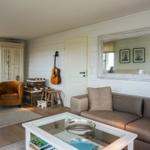 Wohnzimmer mit Sofa, Sessel, Glas-Tisch und Akustikgitarre an der Wand.