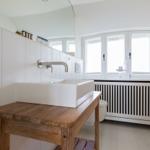 Badezimmer mit Waschtisch auf Holzbank, Fenster und Heizkörper.