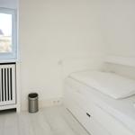 Ein Schlafzimmer mit weißem Bett, Fenster und Heizkörper.