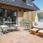 Terrasse mit Tisch, Stühlen und Strandkorb auf Steinplatten.
