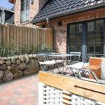 Terrasse mit Tisch, Stühlen und Steinmauer. Hinterhof mit Holzzaun und Backsteinhaus.