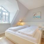 Schlafzimmer mit Dachschrägen, großem Fenster und Bett mit weißen Laken.