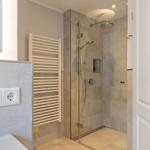 Dusche mit Glaswand, Heizkörper und Steckdosen an der Wand