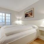 Schlafzimmer mit Doppelbett, Fenster und Nachttisch.