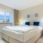 Schlafzimmer mit Doppelbett, Fenster mit Meerblick und Nachttischen mit Lampen.