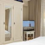 Schlafzimmer mit Kleiderschrank, Fernseher und Fenster mit Vorhängen.
