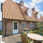 Haus mit Ziegeldach, Terrasse und Gartenmöbel unter blauem Himmel.