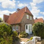 Ein Haus mit rotem Ziegeldach, weißer Tür und umliegenden grünen Sträuchern.