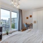 Schlafzimmer mit Bett, Schreibtisch und Balkonansicht.