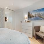 Schlafzimmer mit Bett, Schrank, Kommode und Sessel. Wandbild zeigt Strand.