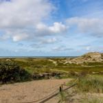 Weg durch Dünenlandschaft mit Blick auf Meer und Himmel.
