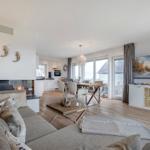 Wohnbereich mit Kamin, Esstisch und TV-Schrank. Blick auf Terrasse und Strand.