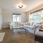 Wohnzimmer mit zwei Sofas, Glas-Tisch und Kamin. Holzboden und große Fenster.
