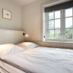 Schlafzimmer mit Bett, Fenster und Wandlampen.
